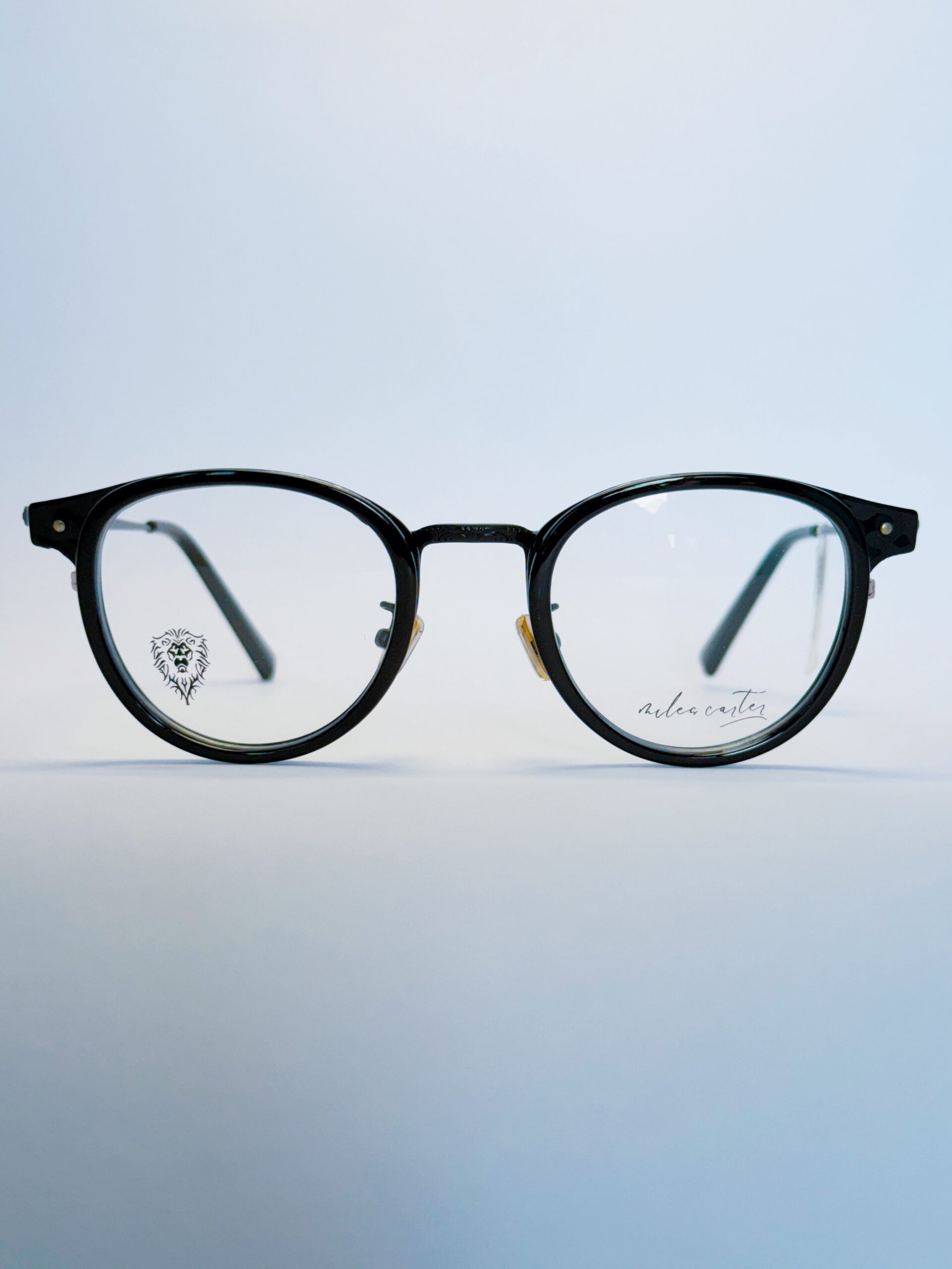 Black round eyeglasses with transparent lenses and metal bridge, displayed on a soft gradient background. Available at www.spexovision.com